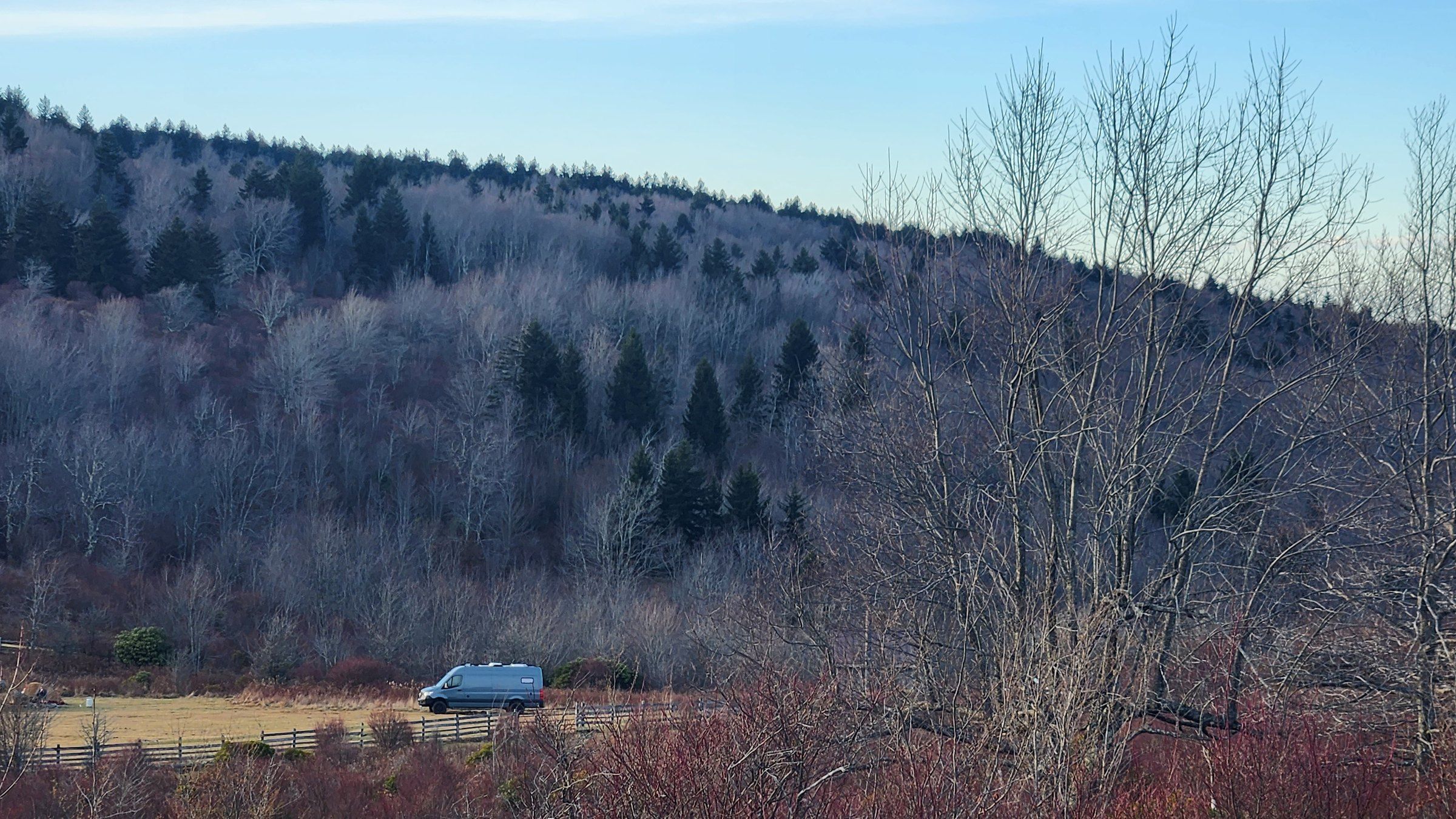 The van small in a wide mountain valley, bare winter trees on the slope.