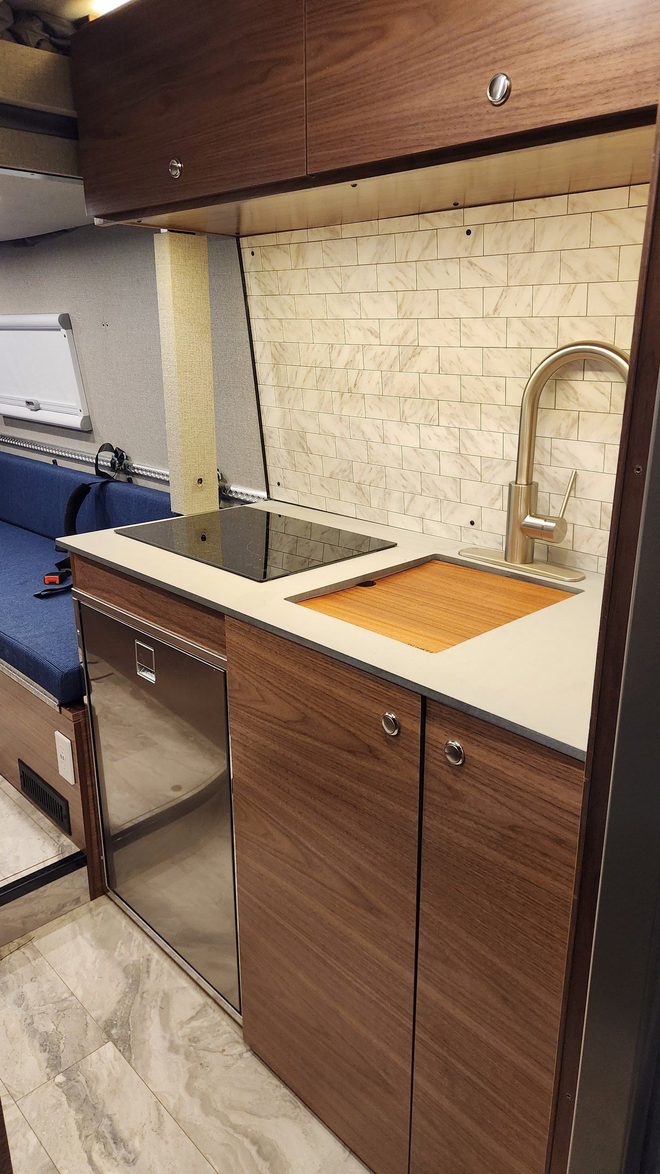 Walnut galley with induction cooktop, sink with cutting board, travertine backsplash.